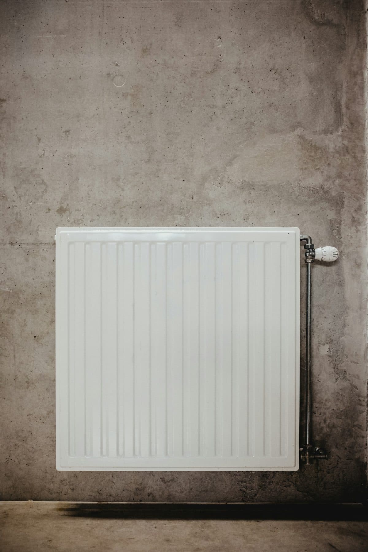 Weißer Heizkörper mit Thermostatkopf an einer Betonwand